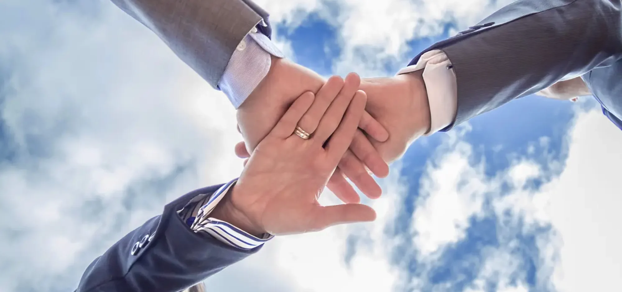 Bottom view of business team showing unity with hands together over blue sky background